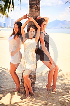 three brunette slim girls lean on palm on beach