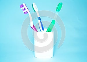 Three brushes for cleaning teeth in a glass white and orange on a blue background. Shaving machines in a glass. Brushes and