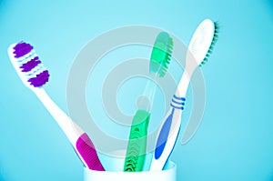 Three brushes for cleaning teeth in a glass white and orange on a blue background. Shaving machines in a glass. Brushes and