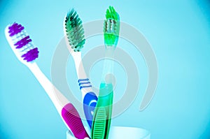 Three brushes for cleaning teeth in a glass white and orange on a blue background. Shaving machines in a glass. Brushes and