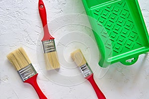 Three brushes with red handles and green paint tray on white concrete background. tools and accessories for home renovation. Top