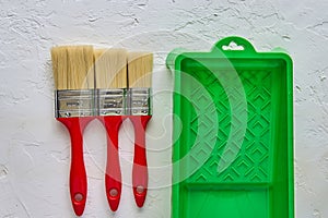 Three brushes with red handles and green paint tray on white concrete background. tools and accessories for home renovation. Top
