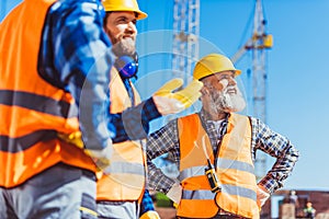 Three builders in reflective vests and hardhats discussing work