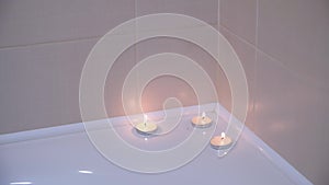 Three burning candles on the edge of bath in bathroom, close-up view.