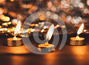 Three burning candles on pile of coins and bokeh in ht ebackground in Deepawali concept