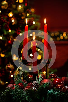Three burning red candles in the dark against the bokeh of a Christmas tree, lights and decorations