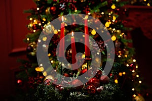 Three burning red candles in the dark against the bokeh of a Christmas tree, lights and decorations