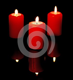 Three burning red candles are reflected in a black mirror background