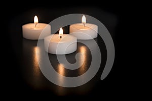 Three burning tea lights on a black background