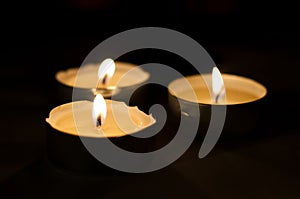 Three burning tea lights on black background