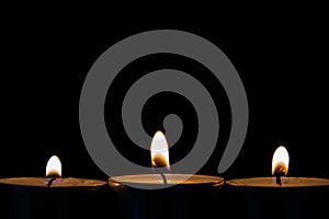 Three burning tea lights on a black background