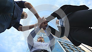Three business men standing outdoor near office and stacked arm together in unity and teamwork. Hands of businessman