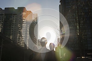 Three business people walking down a city street with sunlight at their back, lens flare