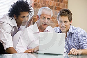 Three businessmen in office looking at laptop