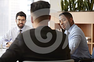 Three Businessmen Sitting Around Table Meeting In Modern Open Plan Office