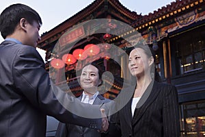 Three businesspeople meeting outdoors with Chinese architecture in background.