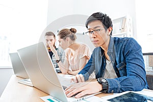 Three businesspeople working in office with laptops