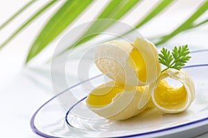 Three Butter curl or roll, on plate front view.greenery in the background