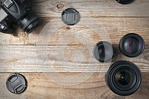 Three camera lenses and a dslr digital camera on a wooden table, top view