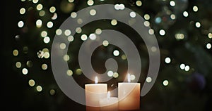 Three candles burn against the backdrop of blurry Christmas tree lights.