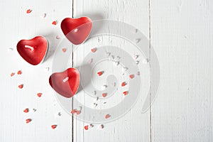 Three candles in the form of red heartbeats on a white background and scattered confetti