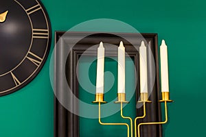 Three candles on a green background, on the wall a clock and a frame