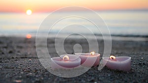 Three candles in shape of heart burn on sand on the sea beach near the sea waves