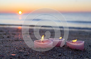Three candles in shape of heart burn on sand on the sea beach near the sea waves