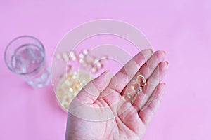 Three capsules of omega three on the female palm on a pink background with a glass of water and fish oil top view