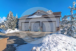 Three car garage with white doors and snowy driveway on a sunny winter day