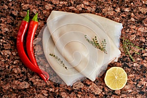 Three carcasses of fresh raw squid with lemon, pepper, thyme on a marble stone dark table