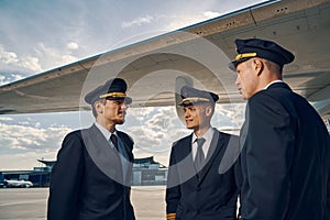 Three Caucasian pilots standing by an airplane wing