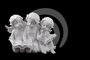 Three ceramic white angels read the book, dreaming and thinking.