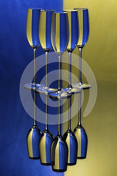 Three champagne glasses on a shiny surface with water that distort yellow and blue background