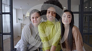 Three charming multiethnic young women posing indoors looking at camera smiling. Portrait of attractive Caucasian