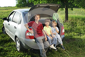 Three cheerful child sitting in the trunk of a car