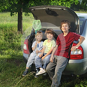 Three cheerful child sitting in the trunk of a car