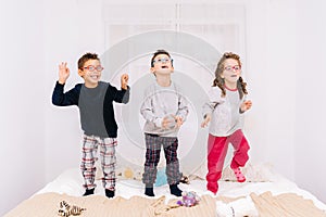 Three cheerful children with glasses jumping and playing on the bed