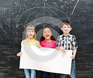 Three cheerful children holding white empty paper sheet
