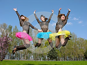 Three cheerful showgirls jumping outdoors