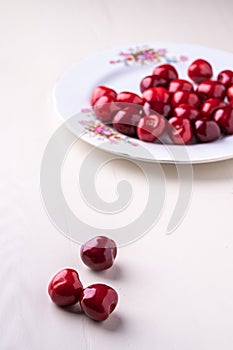 Three cherry berries with white plate with cherries in background on wooden white background angle view