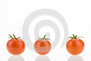Three cherry tomatoes with reflections, on white
