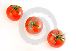 Three cherry tomatoes with stems arranged diagonally isolated on white tabletop background surface, top view