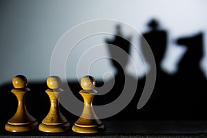 Three chess pawn casting Queen King and Knight shadow in dark concept of strength or aspirations