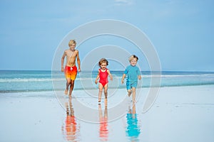 Three children boys and girl run together on sand beach