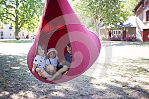 Three children, boys swinging in a big cloth swing in a park