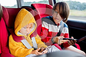 Three children, boys, traveling in car in carseat and playing on mobiles