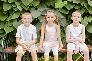 Three children friends sit on bench in summer