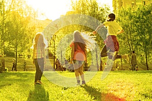 Three children girls at sunset jumping in the park, back view