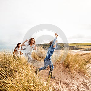 Three Children Having Fun Exploring In Sand Dunes On Winter Beach Vacation